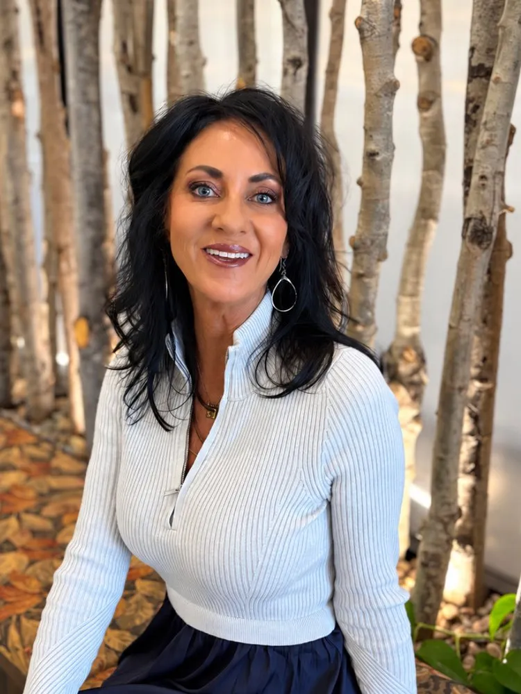 Renee Blanco, smiling, in a light sweater in front of a birch-branch backdrop